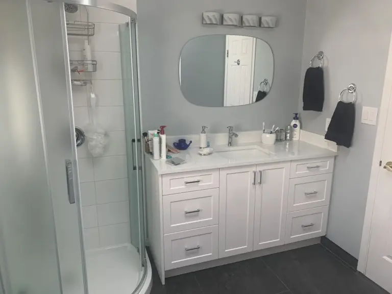 Curved glass shower beside a white shaker vanity with a stone countertop, bathroom renovation in Surrey